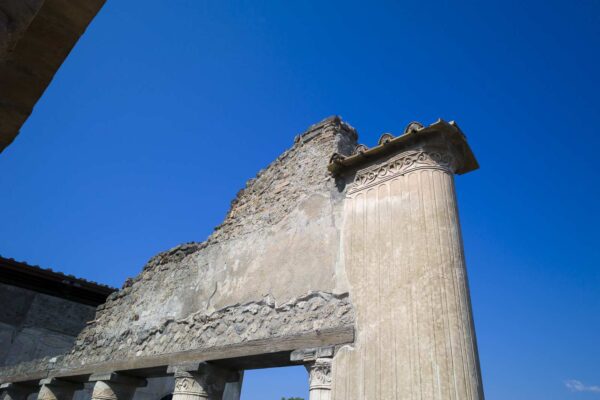Colonne décorée aux thermes de Pompéi avec des détails architecturaux et un ciel bleu.