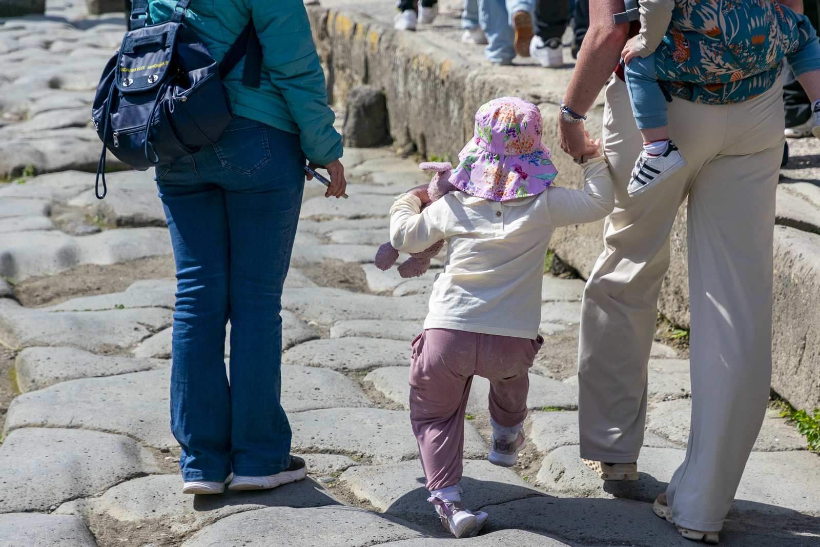 Une petite fille au bonnet rose se promène à Pompéi, tenue par la main d'un adulte