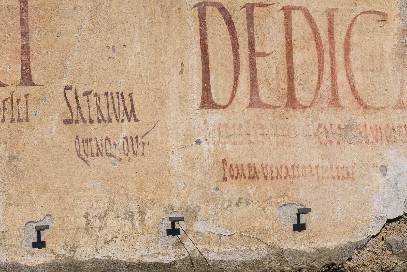 Inscription latine sur un mur ancien, avec des lettres rouges et noires sur fond beige.