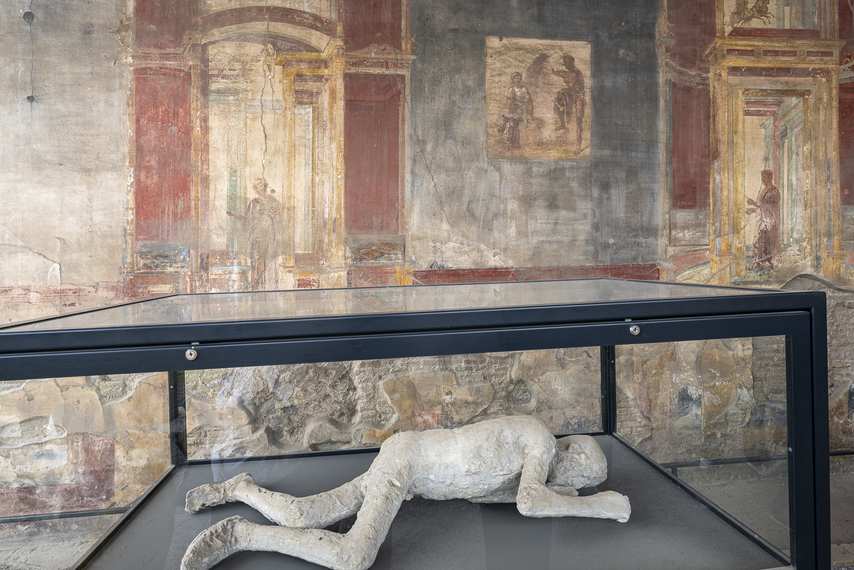 Plaster cast of a victim of Pompeii's eruption displayed in the Macellum, with frescoes on the walls
