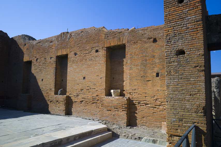 Detail of the brick wall of the municipal buildings in Pompeii, with niches and archaeological fragments.