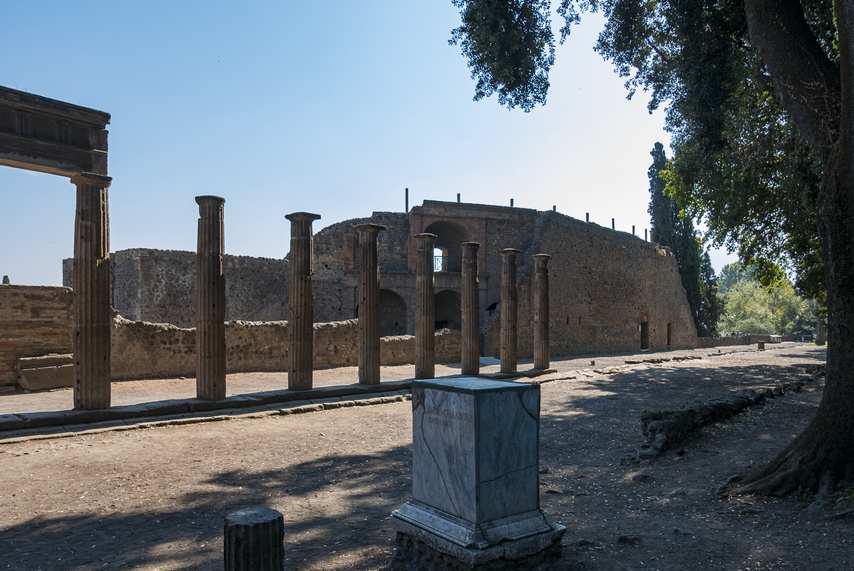 Wide view of the Triangular Forum of Pompeii with columns, surrounding wall and shady trees