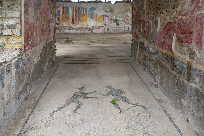 Roman mosaic with two wrestlers in the Palestra dei Iuvenes in Pompeii, with colorful frescoes in the background