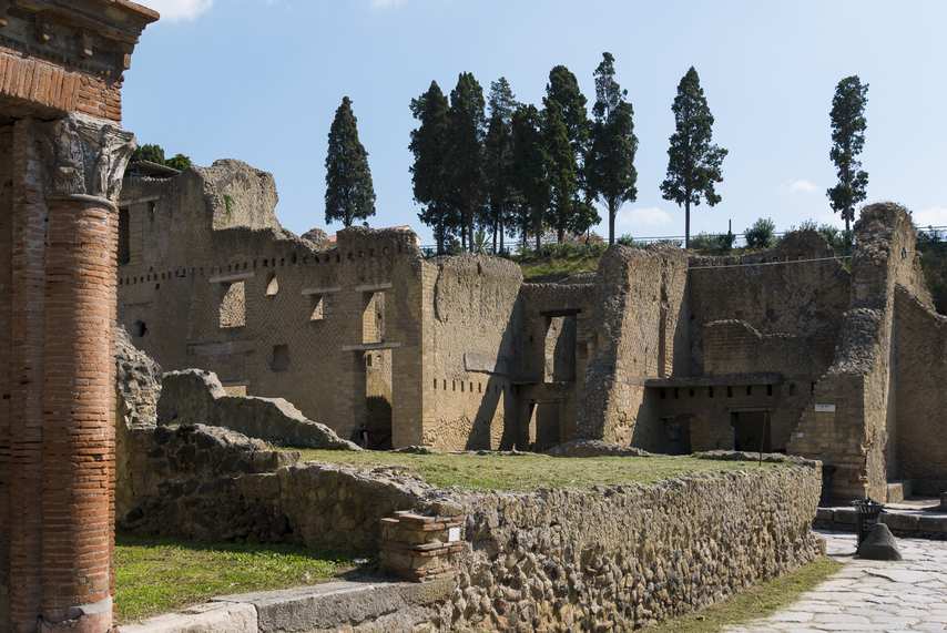 Roman ruins of the Herculaneum Archaeological Park with cypress trees in the background