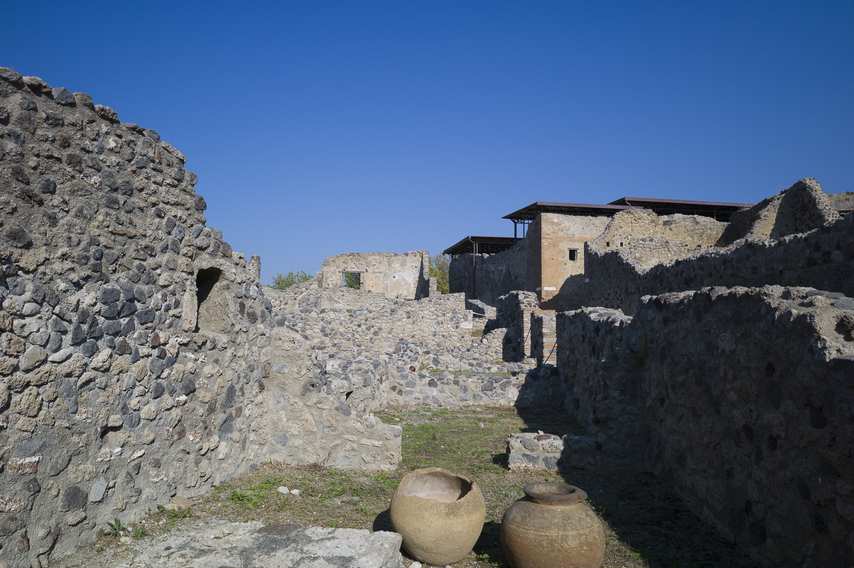 Pompeii ruins with amphorae in the foreground and remains of stone walls under a clear sky