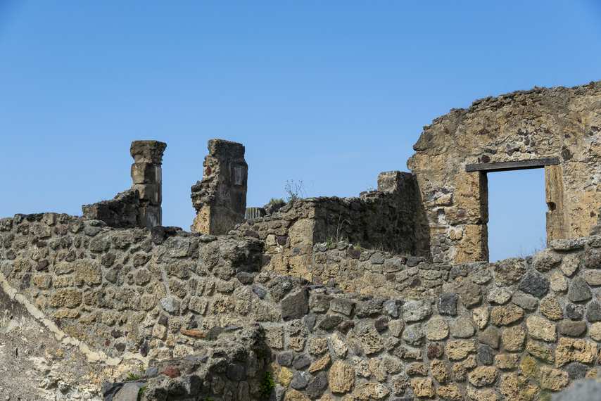 Ancient walls and partially preserved columns among the ruins of Pompeii under a blue sky