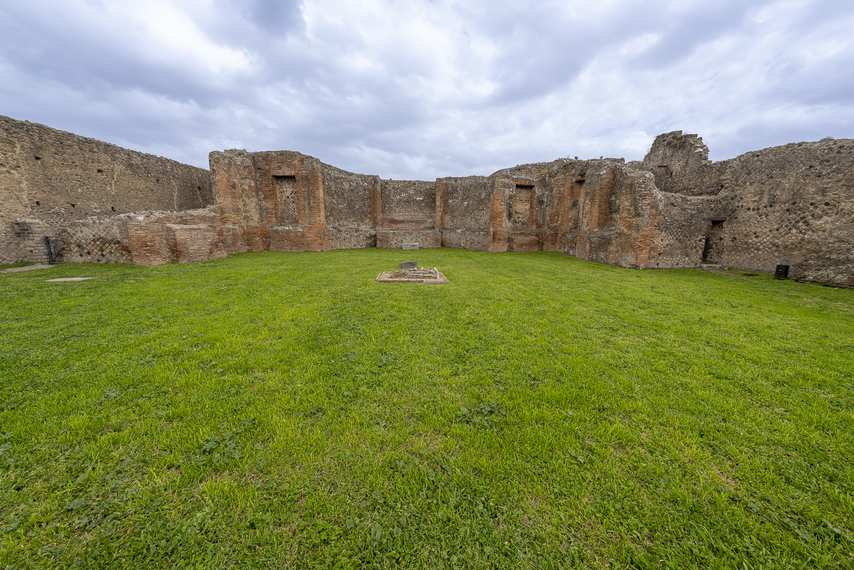 Ruins of the Sanctuary of the Public Lares in Pompeii with green lawn and wall structure