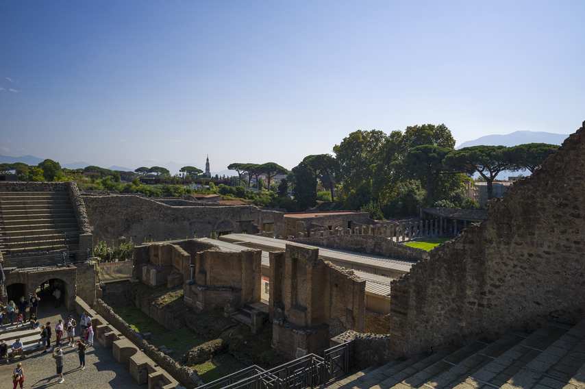 Vue de la scène et de l’arrière du Grand Théâtre de Pompéi, avec des arbres et le Quadriportique en arrière-plan